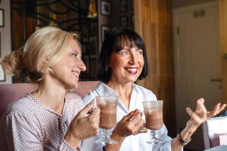 Two happy mature smiling women chatting while having lunch in cafe. Leisure concept of mature peopleの写真素材