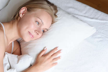 Beautiful young blonde woman waking up in the morning in a white bed. Self care lifestyle conceptの写真素材