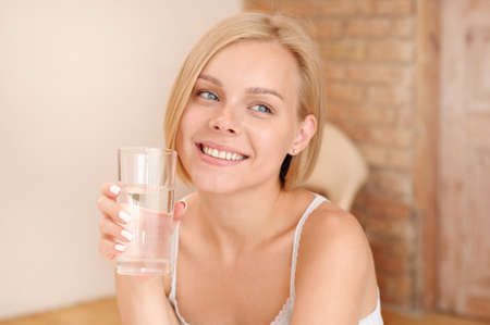 Beautiful smiling young blonde woman waking up and drinking water in the morning. Healthy lifestyle conceptの写真素材