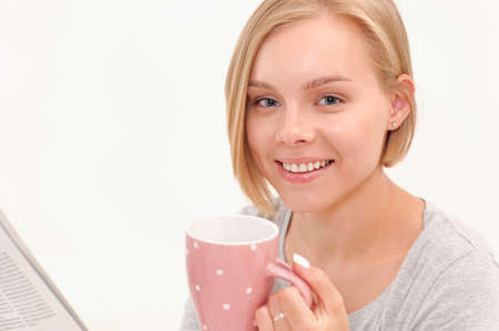 Beautiful smiling young blonde woman drinking coffee and reading newspaper in the morning. Healthy lifestyle conceptの写真素材