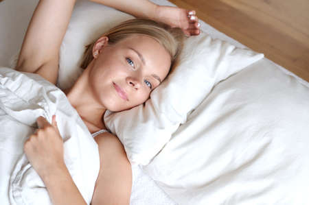 Beautiful young blonde woman waking up in the morning in a white bed. Self care lifestyle conceptの写真素材