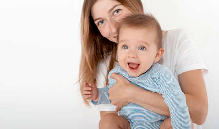 Mother holding cute happy baby boy with beautiful blue eyes on white background. Happy childhood and motherhood concept.の写真素材