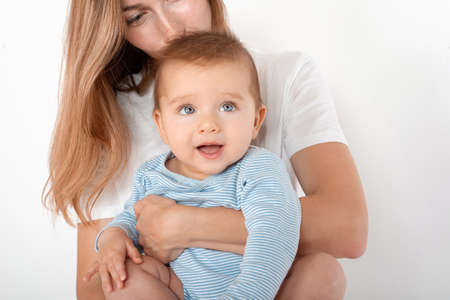 Mother holding cute happy baby boy with beautiful blue eyes on white background. Happy childhood and motherhood concept.の写真素材
