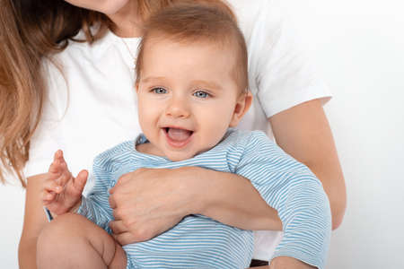 Mother holding cute happy baby boy with beautiful blue eyes on white background. Happy childhood and motherhood concept.の写真素材