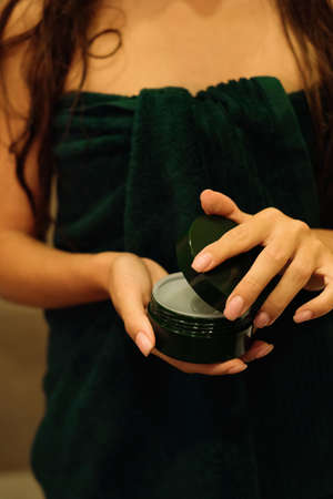 Young woman in a towel holds a jar with a cosmetic cream in her hands. Skin care products. Beauty spa concept.の写真素材