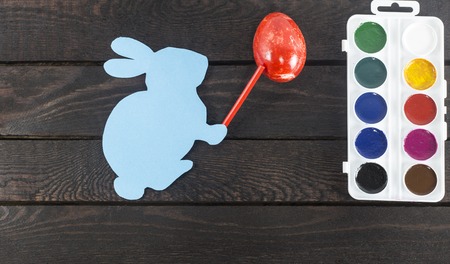 card bunny with marker on it's hand, painting egg into red on dark brown wooden backgroundの写真素材