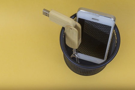 Electronic equipments in trash can on yellow background.