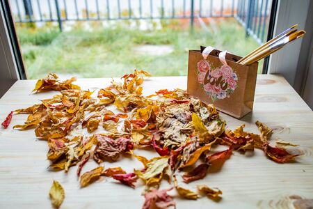 Art concept of autumn composition. Paper bag with autumn yellow dried leaves on a wooden tableの写真素材