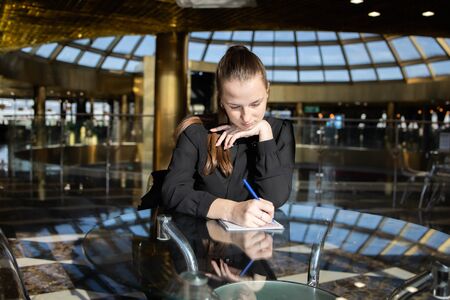 Business girl in black sits thoughtfully at a table and fills a documentの写真素材