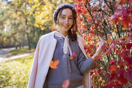 The girl in glasses stands on a background of red autumn leaves in the fall. Autumn leaves fall on a girlの写真素材