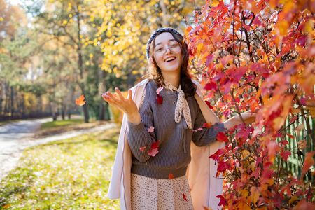Beautiful woman in glasses throws up red autumn leaves and smiles. Happy woman throws red autumn leavesの写真素材