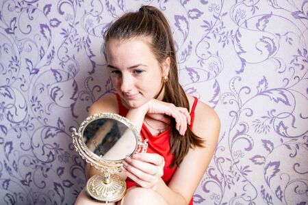young girl looks in a small vintage mirror on a vintage wall backgroundの写真素材