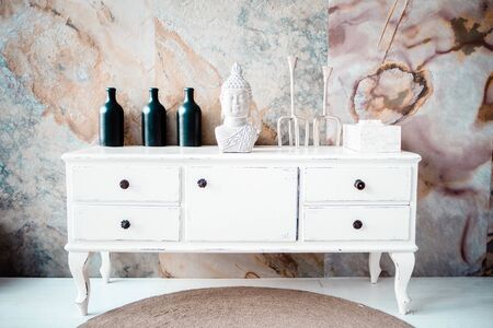 a new white dresser against the backdrop of an abstract wall. Buddha's head next to vases on the dresser.の写真素材