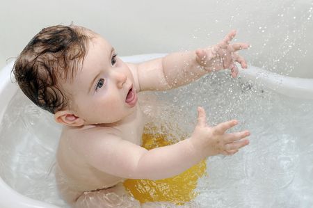 Cute baby playing with water in white tubの写真素材