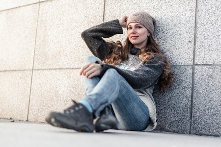 Young woman sitting alone next to granite wall, looking at cameraの写真素材