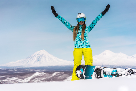Happy young woman with snowboard in front of volcanos. Russia, Kamchatka peninsulaの写真素材