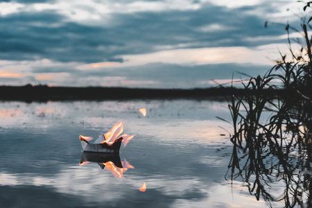 White paper boat on fire floating in the river at sunsetの写真素材