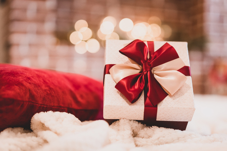 Wrapped gift with red ribbon on fireplace background at home.の写真素材