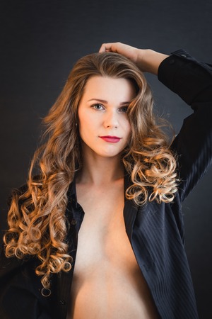 Portrait of a young woman with curly hair in a black shirt on dark background
