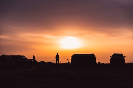 Silhouette of a man standing in a camping site at sunset