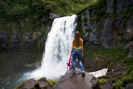 Female hiker standing if front of the waterfall. Traveling through Kamchatka peninsula, Russia