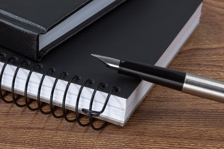 A fountain pen and black notebooks on wooden texture imitating a desk.