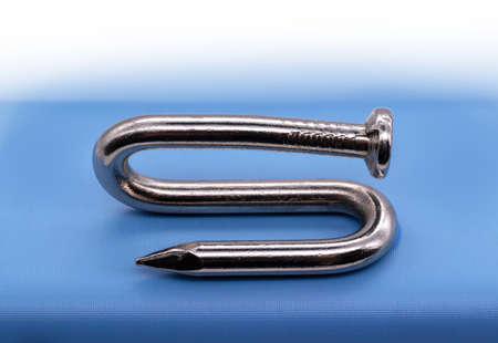 Bent metal nail on blue texture background. Single perfectly object, macro detail.