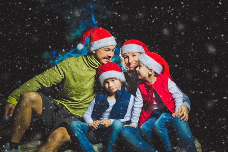 Portrait of friendly family in Santa caps looking at camera on Christmas evening with snowの写真素材