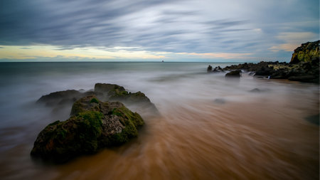 Large body of water with rocks in the foreground, long exposure shot.の素材