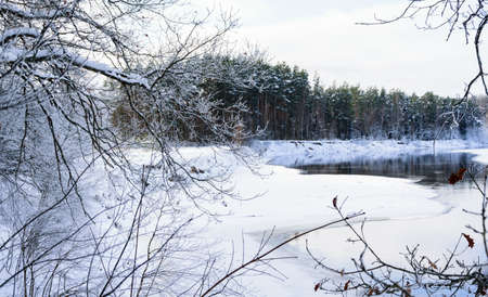 There is a lot of snow, a coniferous forest and a river with steam rising from the water.