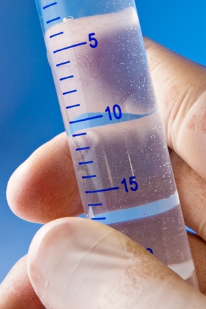 Hand with gloves holding research cylinder filled with liquid on blueの写真素材