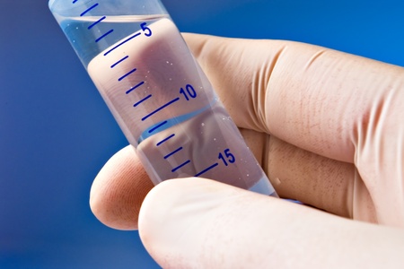 Hand with gloves holding research cylinder filled with liquid on blue