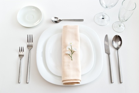 place setting with white plates forks glasses beige napkin and little flowerの写真素材