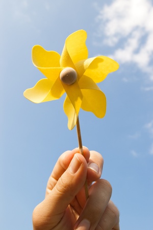 hand with yellow pinwheel on clear blue skyの写真素材