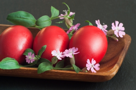 three red Easter eggs with little flowers in wood bowlの写真素材