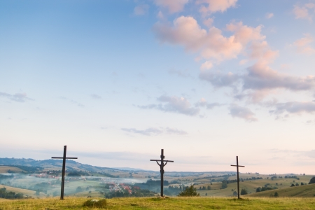 three crosses against  sky and village on hillsの写真素材