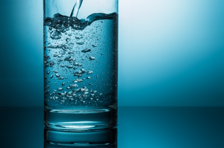 pouring water in glass closeup in blue lightの写真素材