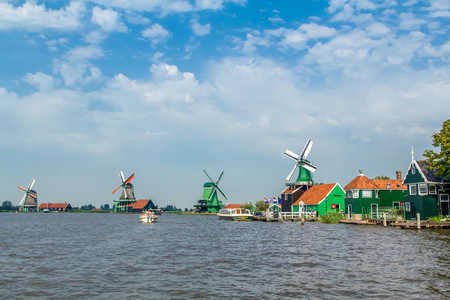 The famous historical windmills on the water at the Zaanse Schans on a blue and cloudy day in Zaandam in the Netherlands.の写真素材