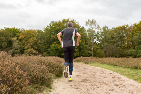 Back of an elderly man running on a sandy path at the Blaricummerheide in the Netherlands.の写真素材