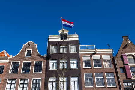 Dutch flags on the canal houses with a blue sky in the center of Amsterdam in the Netherlands.の写真素材