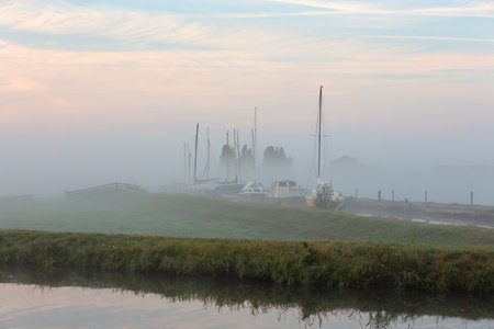 Sailboats and motor yachts moored in a harbor (Botersloot) in the middle of the meadows on a foggy morning in the South-Holland town of Warmond in the Netherlands.の写真素材
