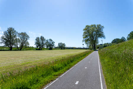 A neatly 2 lane asphalted cycle path along the A44 and the freshly mowed meadows towards Sassenheim train station in the South-Holland municipality of Teylingen on a sunny day in the Netherlands.の写真素材