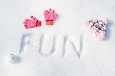 Word "FUN" written on fresh snow, with pink gloves, cap and snowball.の写真素材