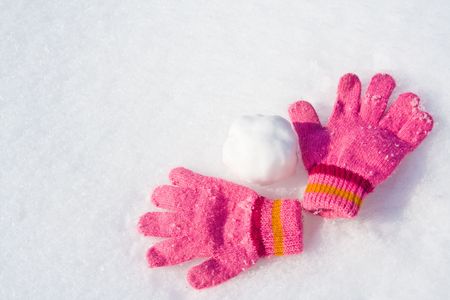 Warm female pink gloves and snowball on fresh snow.の写真素材