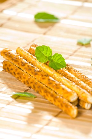 Salty sesame sticks on table cover with mint leaves.