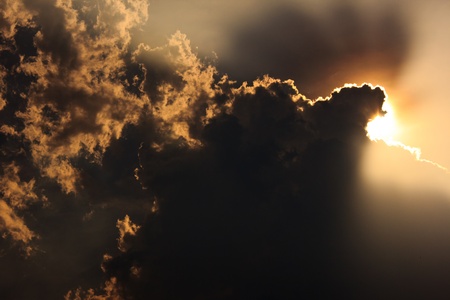 sun behind cloud with orange beam spread around