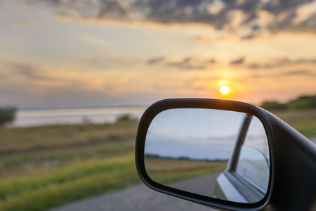 Sunset landscape reflected in rear view mirror of driving car.の写真素材