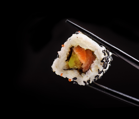 Closeup of traditional japanese sushi roll with salmon and tuna fish on bamboo chop sticks over black background. Sushi bar menu design with copyspace.の写真素材