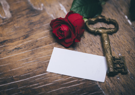 Valentine's day still life concept. Valentine gift, red rose, vintage key and empty greeting card on wooden table. Valentine holiday design.の写真素材