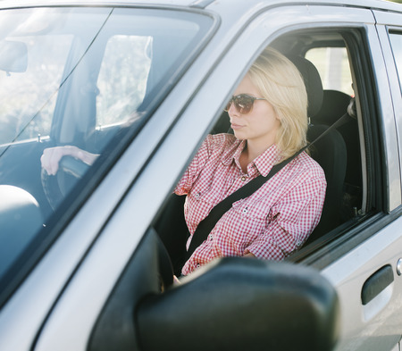 Young blond woman driving a car. Casual girl with sunglasses traveling in vehicle.の写真素材